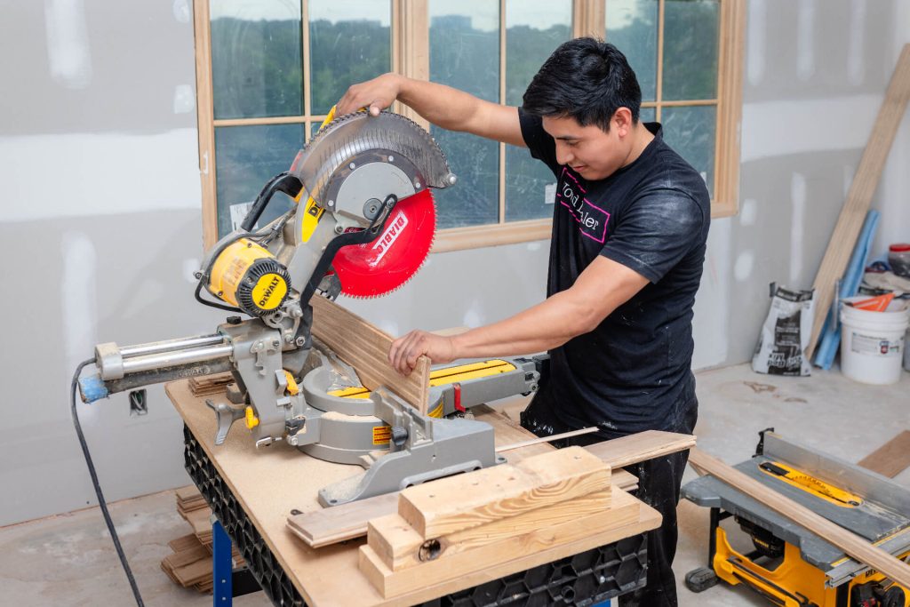 Installer cutting hardwood board with miter saw during subfloor prep